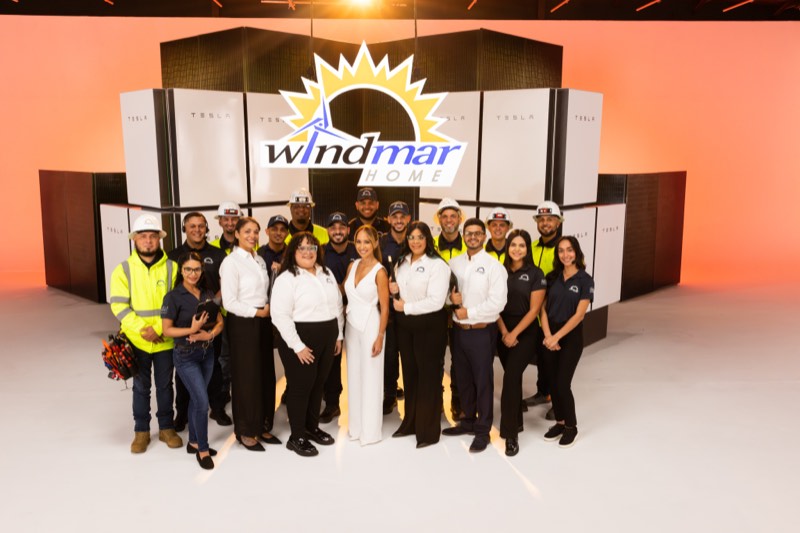 Equipo completo de WindMar Home — instaladores, ingenieros y ejecutivos — frente a una pared de baterías Tesla Powerwall con el logo WindMar al centro